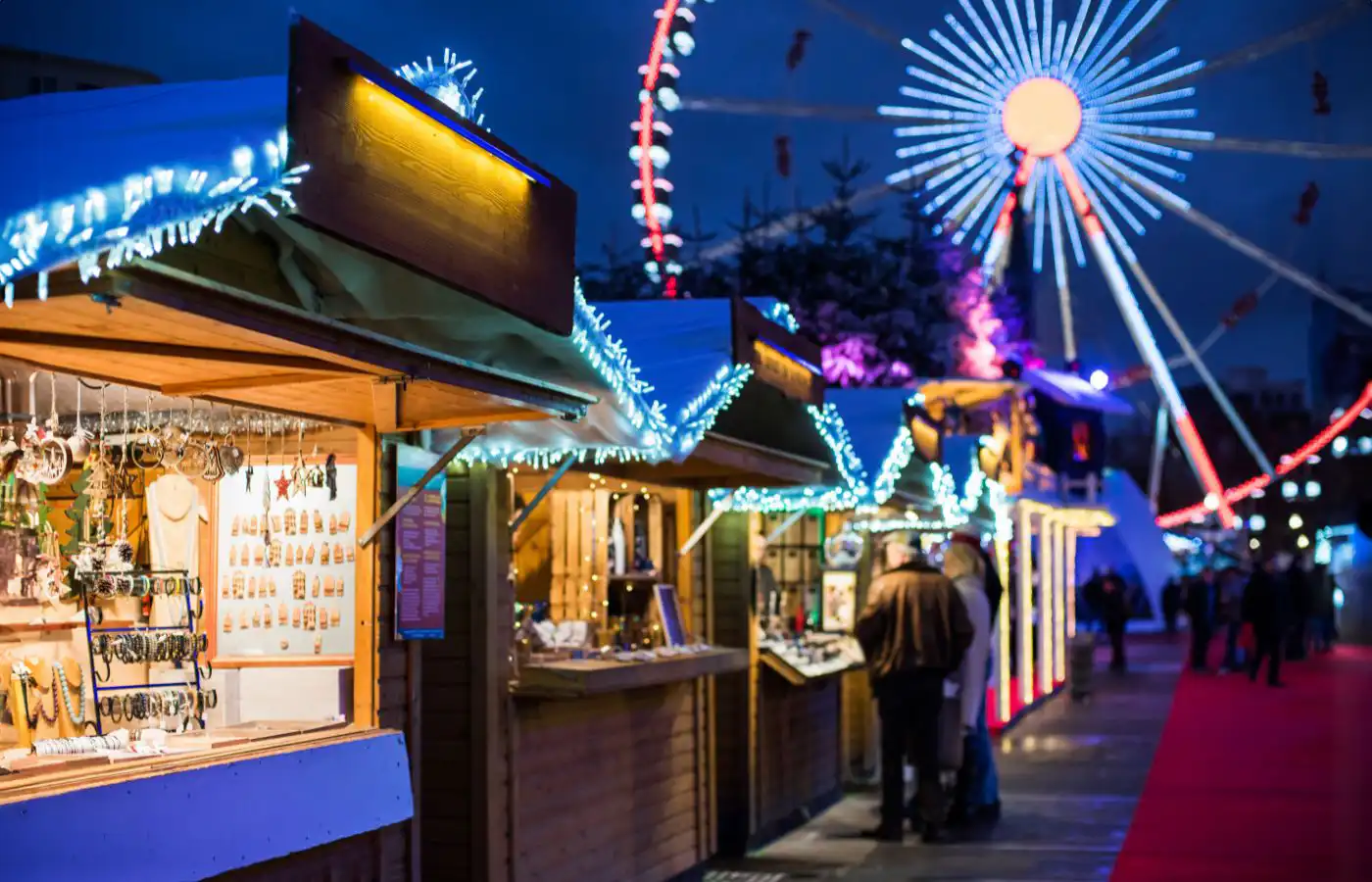 Verlichte chalets van de kerstmarkt in Brussel met feestelijke decoraties, met op de achtergrond een verlichte reuzenrad, tijdens het evenement Plaisirs d'Hiver.