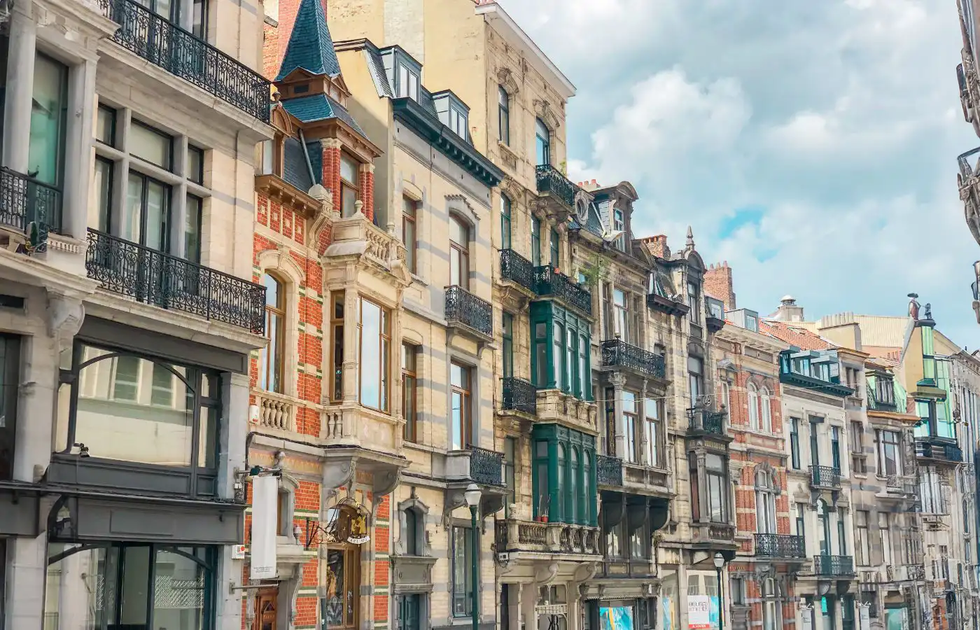 Rij van traditionele Brusselse herenhuizen met karakteristieke gevels en architecturale details, onder een heldere lucht met enkele wolken.